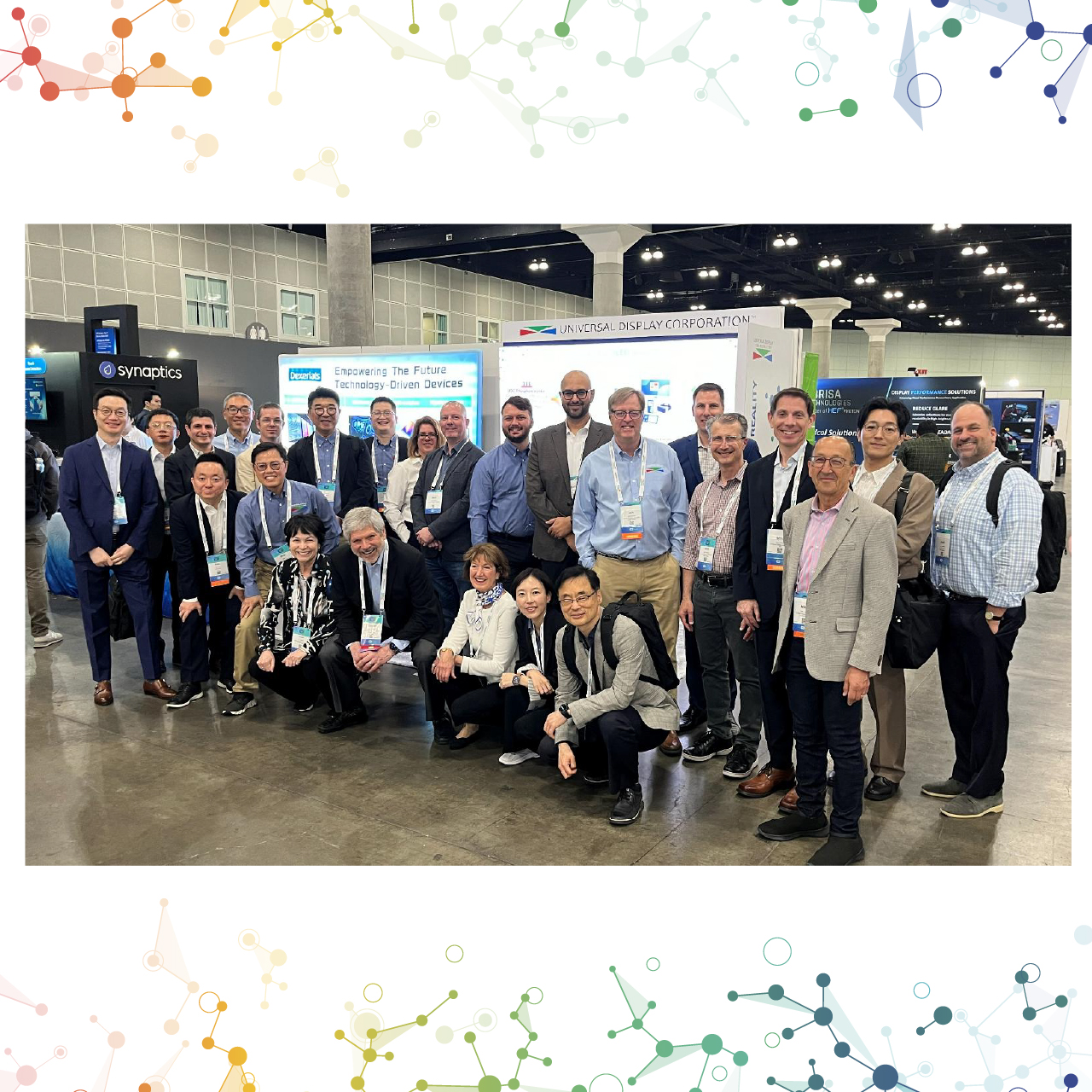 A group of UDC employees standing in front of the Company's booth at SID Display Week 2026.